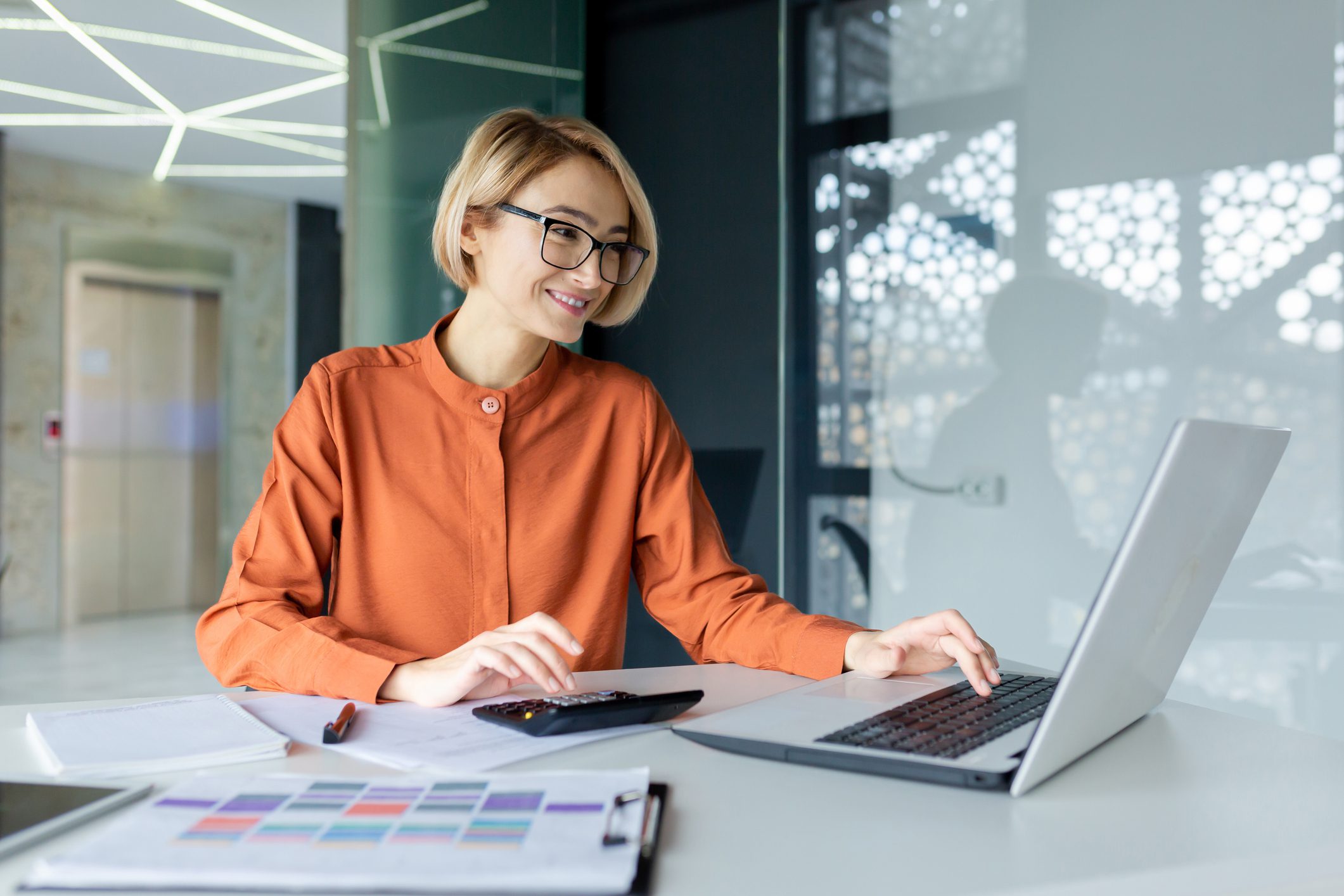 Woman works on laptop and calculator.